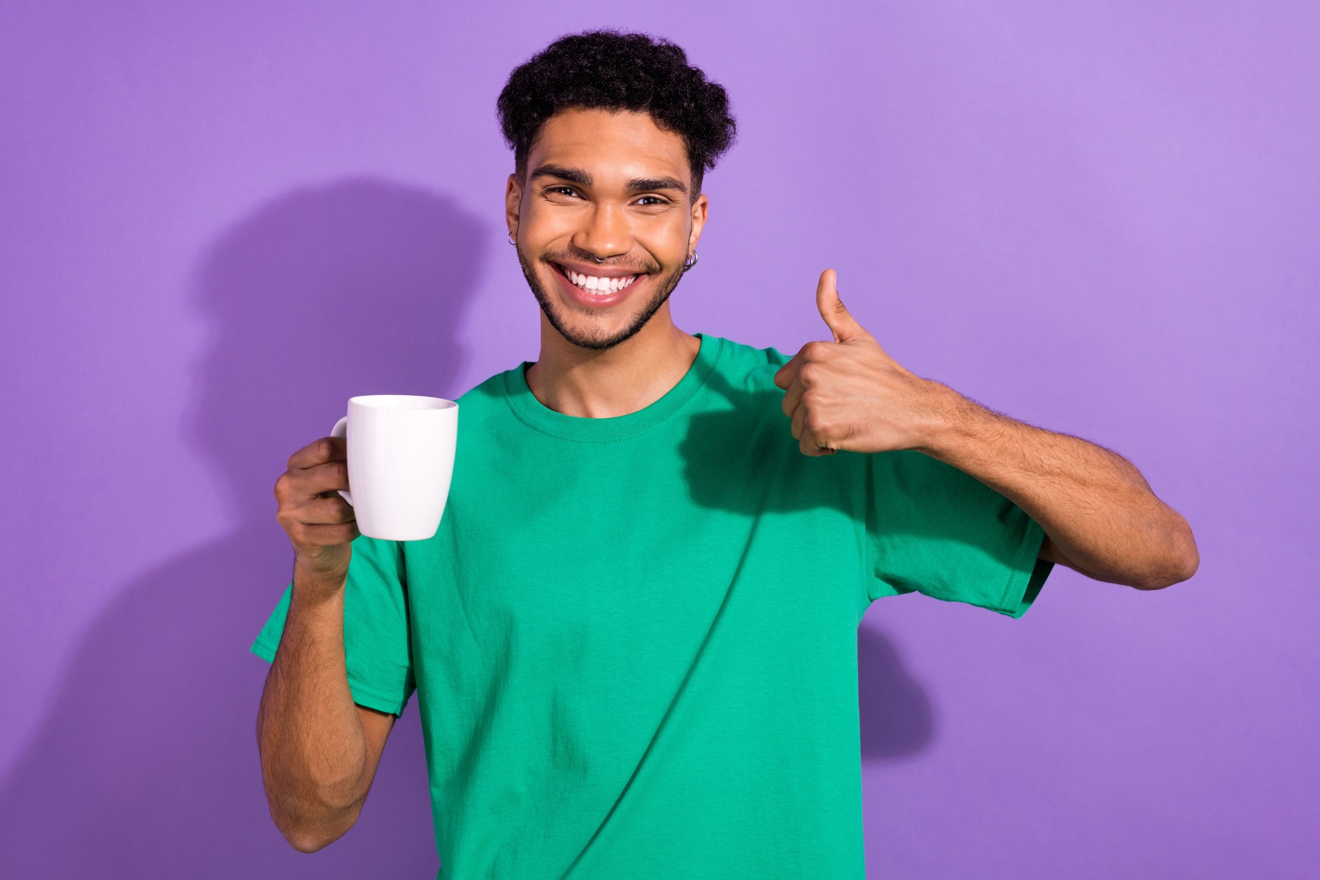 Photo of charming attractive man wear green t-shirt drinking cacao showing thumb up isolated purple color background